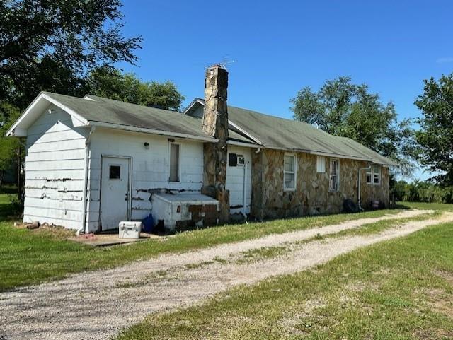 12074 S 1600th Rd, Nevada, MO 64772 - back of house with a chimney, dirt driveway, and a lawn