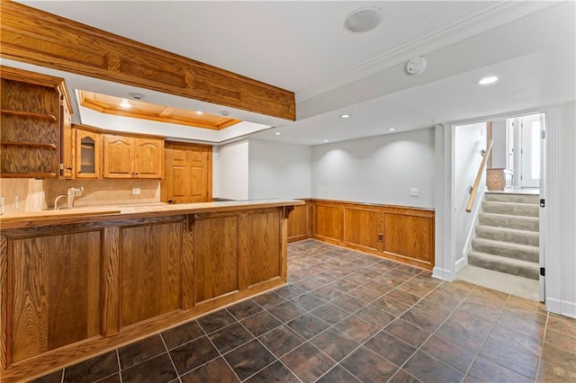 1103 N 2nd St E, Louisburg, KS 66053 - kitchen featuring crown molding, glass insert cabinets, a peninsula, brown cabinetry, and a wainscoted wall