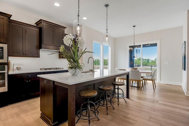 16567 W 170th St, Olathe, KS 66062 - kitchen with stainless steel appliances, a center island with sink, light wood finished floors, a kitchen breakfast bar, and light countertops