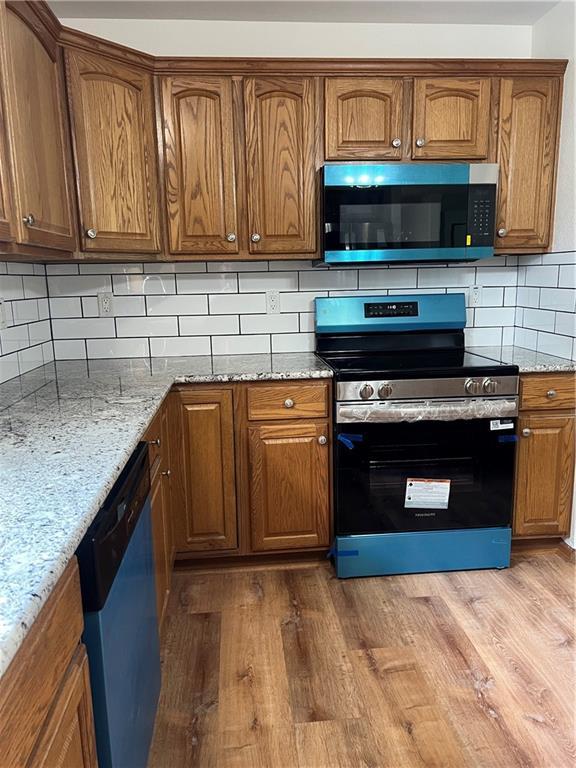 36987 W 63rd St, Camden, MO 64017 - kitchen featuring stainless steel appliances, brown cabinets, light stone countertops, and wood finished floors