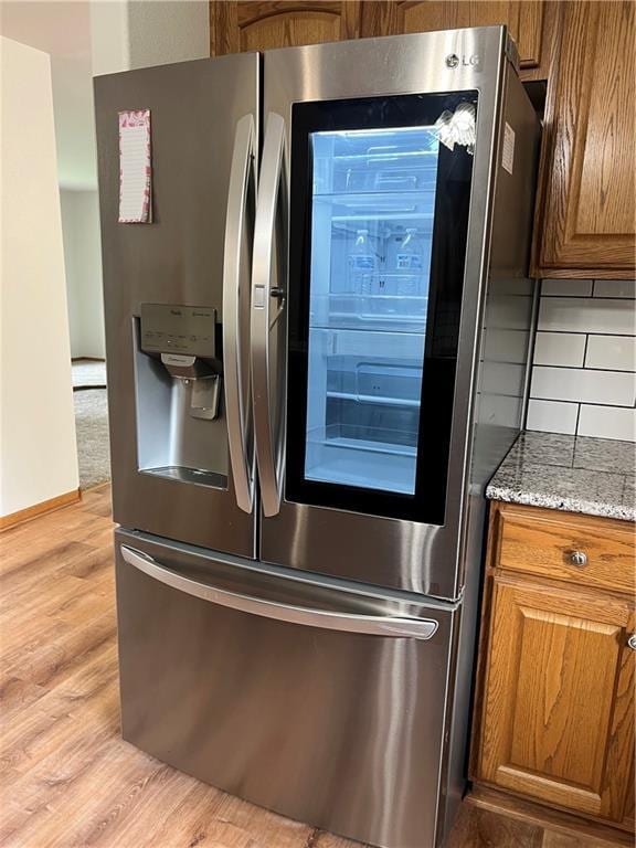 36987 W 63rd St, Camden, MO 64017 - kitchen view of stainless steel refrigerator with ice dispenser, brown cabinets, light wood-style floors, and light stone counters