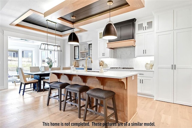 11275 S Gleason Rd, Olathe, KS 66061 - kitchen featuring a raised ceiling, light wood-style flooring, a kitchen island with sink, and light countertops
