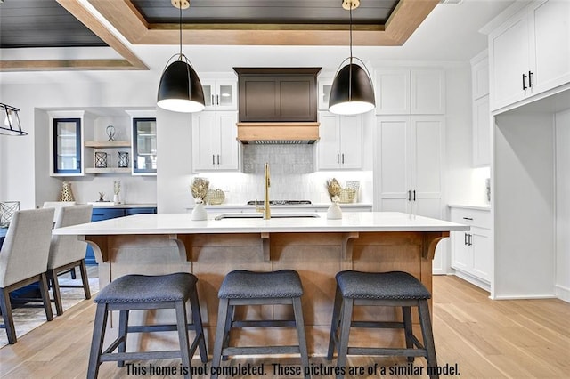 11275 S Gleason Rd, Olathe, KS 66061 - kitchen with a tray ceiling, light countertops, light wood-style flooring, backsplash, and a kitchen island with sink