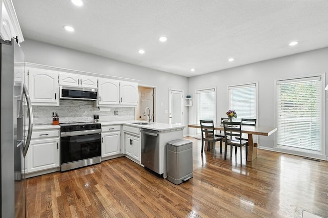 5136 NE Ash Grove Dr, Lees Summit, MO 64064 - kitchen with appliances with stainless steel finishes, a peninsula, dark wood-style flooring, white cabinets, and backsplash