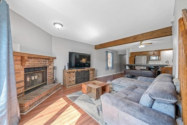 518 NE 6th St Unit A, Blue Springs, MO 64014 - living area featuring light wood finished floors, beamed ceiling, a brick fireplace, and a ceiling fan