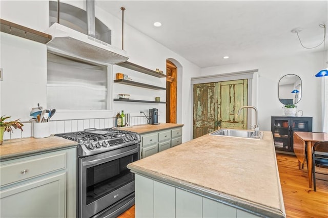 1637 Jefferson St, Kansas City, MO 64108 - kitchen featuring stainless steel gas range oven, light wood-style floors, wall chimney range hood, a center island with sink, and light countertops