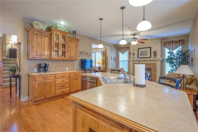 1105 Blazing Star Dr, Lees Summit, MO 64081 - kitchen with stainless steel dishwasher, light countertops, a tile fireplace, glass insert cabinets, and brown cabinets