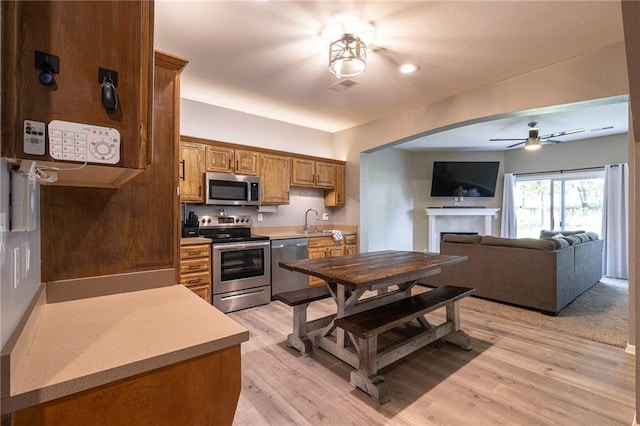 632 SW Shadow Glen Ct, Blue Springs, MO 64015 - kitchen featuring appliances with stainless steel finishes, a ceiling fan, a fireplace, light countertops, and brown cabinetry