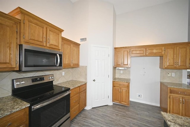 12905 Ridgeview Dr, Platte City, MO 64079 - kitchen with appliances with stainless steel finishes, brown cabinetry, dark wood-style flooring, decorative backsplash, and a high ceiling