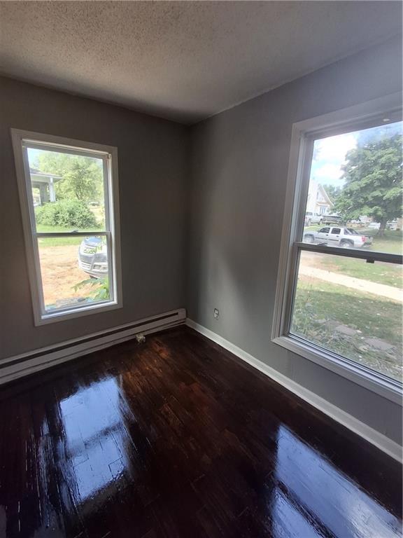 608 N Cedar St, Ottawa, KS 66067 - unfurnished room with a baseboard radiator, dark wood-type flooring, plenty of natural light, and a textured ceiling