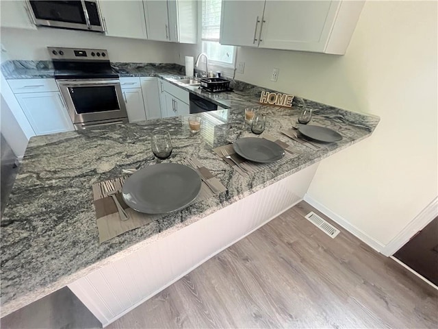 14948 Lakeside Dr, Excelsior Springs, MO 64024 - kitchen with appliances with stainless steel finishes, wood finished floors, dark stone counters, and a peninsula