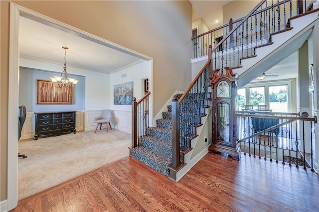 10963 S Carbondale St, Olathe, KS 66061 - stairs featuring wood finished floors, a chandelier, a decorative wall, a wainscoted wall, and ornamental molding