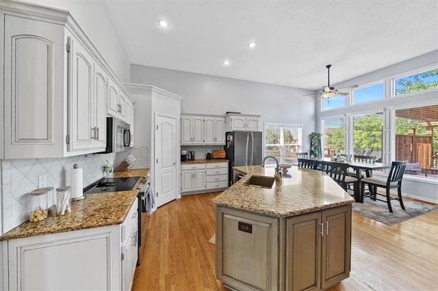 2312 SW Post Oak Ct, Lees Summit, MO 64082 - kitchen with appliances with stainless steel finishes, a center island with sink, ceiling fan, light wood-style floors, and decorative backsplash