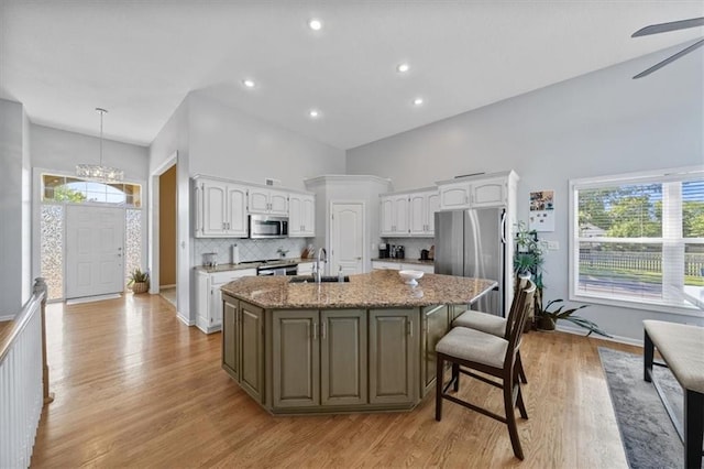 2312 SW Post Oak Ct, Lees Summit, MO 64082 - kitchen featuring stainless steel appliances, white cabinetry, an island with sink, light wood-style flooring, and tasteful backsplash