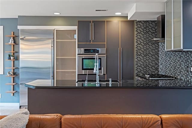 1303 W 47th St, Kansas City, MO 64112 - kitchen featuring stainless steel appliances, wall chimney exhaust hood, glass insert cabinets, a peninsula, and dark stone counters