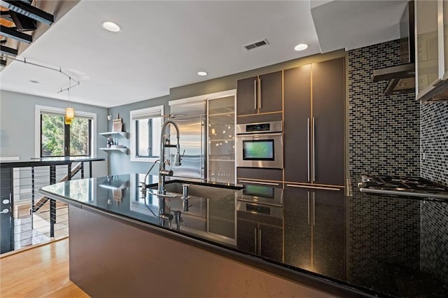 1303 W 47th St, Kansas City, MO 64112 - kitchen with appliances with stainless steel finishes, tasteful backsplash, light wood-style floors, decorative light fixtures, and dark brown cabinetry
