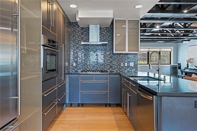 1303 W 47th St, Kansas City, MO 64112 - kitchen featuring stainless steel appliances, light wood-type flooring, a peninsula, wall chimney exhaust hood, and glass insert cabinets