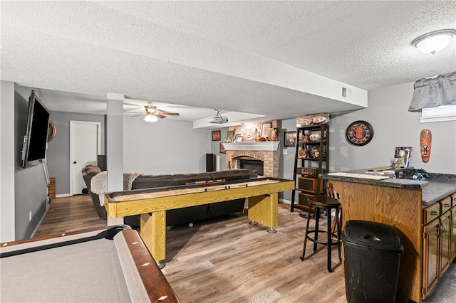 17507 E 35th Ter, Independence, MO 64055 - recreation room featuring a textured ceiling, light wood-type flooring, a brick fireplace, a ceiling fan, and a bar