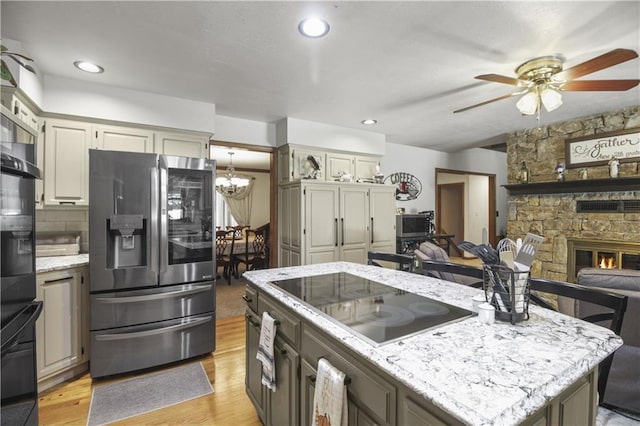 2005 NW Fawn Dr, Blue Springs, MO 64015 - kitchen featuring black appliances, light wood-style floors, a chandelier, a ceiling fan, and a stone fireplace