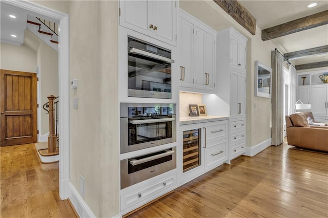 10400 Howe Dr, Leawood, KS 66206 - kitchen featuring wine cooler, light wood finished floors, white cabinets, beamed ceiling, and light countertops