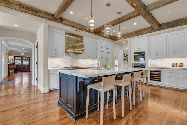 10400 Howe Dr, Leawood, KS 66206 - kitchen with light wood finished floors, arched walkways, a kitchen breakfast bar, custom range hood, and an island with sink