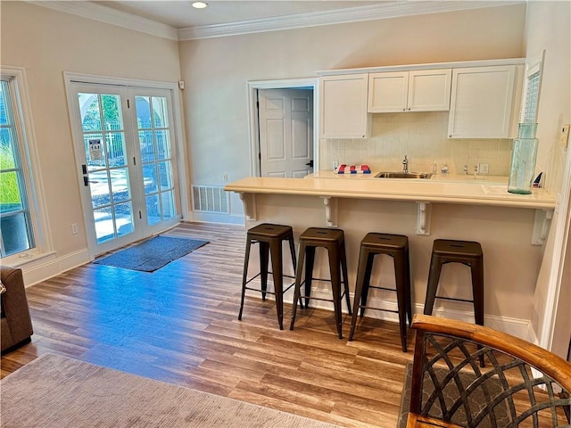 10400 Howe Dr, Leawood, KS 66206 - kitchen featuring a kitchen bar, ornamental molding, white cabinets, decorative backsplash, and light wood-type flooring