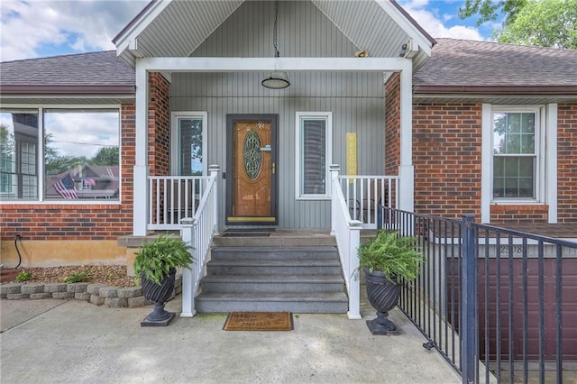 2508 N Mcbride Ave, Sugar Creek, MO 64050 - doorway to property with roof with shingles, brick siding, and covered porch