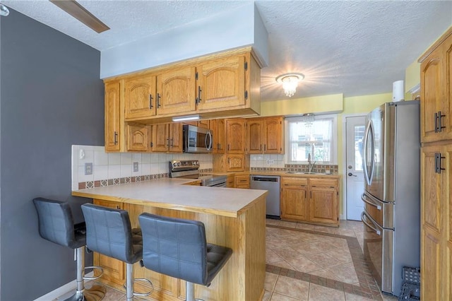 2508 N Mcbride Ave, Sugar Creek, MO 64050 - kitchen with stainless steel appliances, a peninsula, a textured ceiling, decorative backsplash, and a kitchen breakfast bar