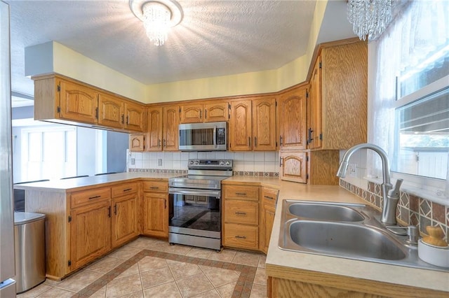 2508 N Mcbride Ave, Sugar Creek, MO 64050 - kitchen featuring stainless steel appliances, light countertops, decorative backsplash, a textured ceiling, and brown cabinets