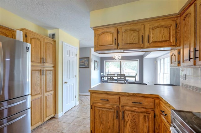 2508 N Mcbride Ave, Sugar Creek, MO 64050 - kitchen with appliances with stainless steel finishes, a peninsula, light tile patterned floors, brown cabinets, and a textured ceiling