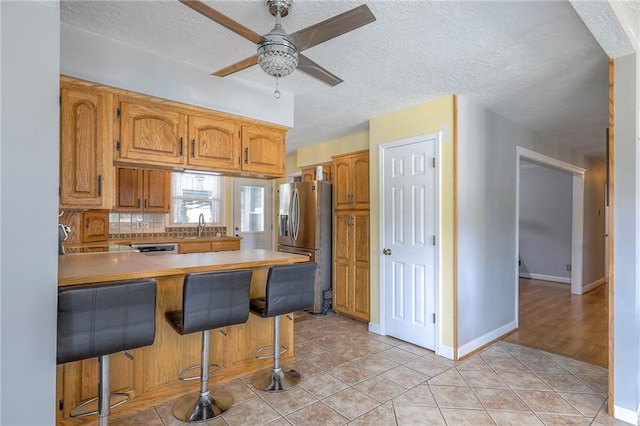 2508 N Mcbride Ave, Sugar Creek, MO 64050 - kitchen featuring stainless steel refrigerator with ice dispenser, a peninsula, a ceiling fan, a breakfast bar area, and backsplash