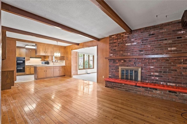 3300 W 93rd St, Leawood, KS 66206 - unfurnished living room with beam ceiling, a brick fireplace, light wood-style floors, and a textured ceiling