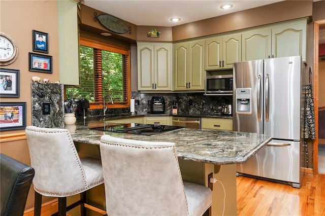 731 E 1100th Rd, Baldwin City, KS 66006 - kitchen with appliances with stainless steel finishes, a peninsula, light wood-style flooring, a breakfast bar, and decorative backsplash