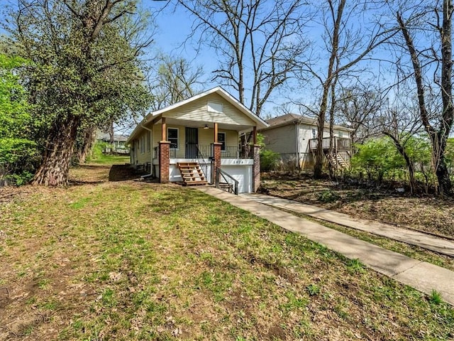3928 E 58th St, Kansas City, MO 64132 - bungalow-style house featuring covered porch, stairway, driveway, an attached garage, and a front yard