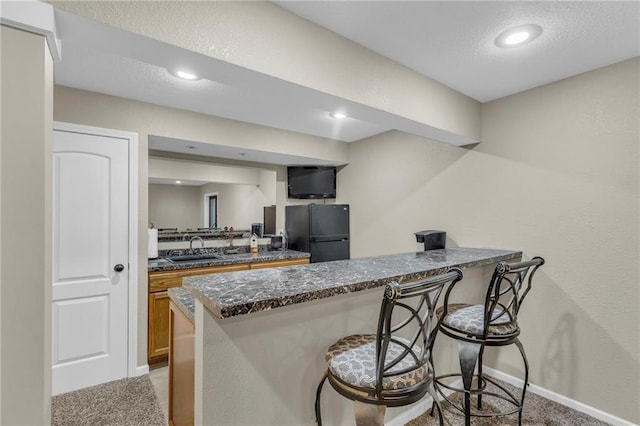 23968 Eagle Ct, Paola, KS 66071 - kitchen featuring freestanding refrigerator, light colored carpet, a peninsula, a breakfast bar, and brown cabinets