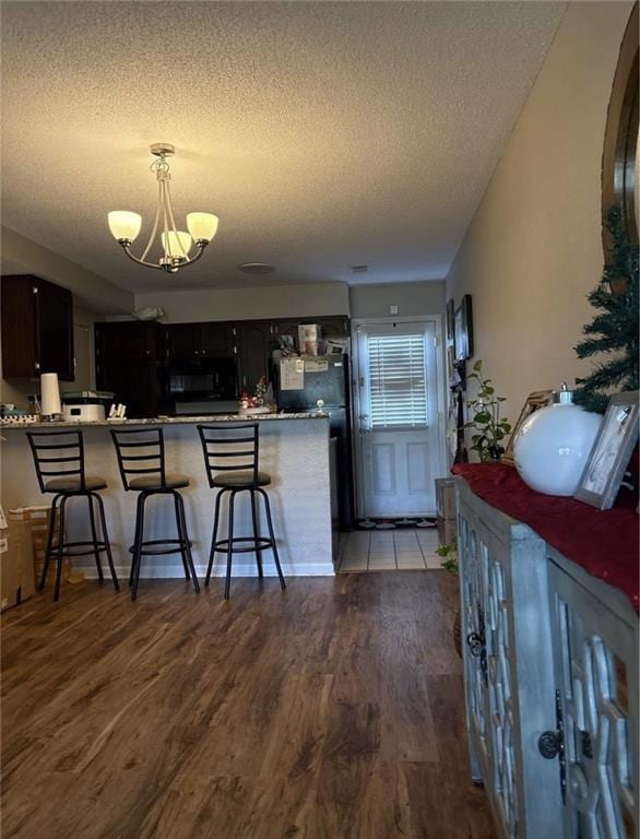 1529 E 120th St, Olathe, KS 66061 - kitchen featuring a textured ceiling, wood finished floors, a kitchen breakfast bar, a chandelier, and a peninsula