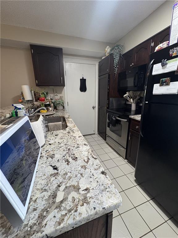 1529 E 120th St, Olathe, KS 66061 - kitchen with black appliances, light tile patterned flooring, light stone counters, dark brown cabinets, and a peninsula