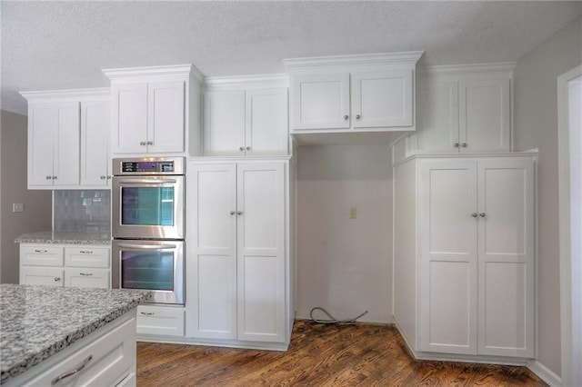 11512 Hadley St, Overland Park, KS 66210 - kitchen with stainless steel double oven, white cabinets, light stone countertops, dark wood-style flooring, and backsplash