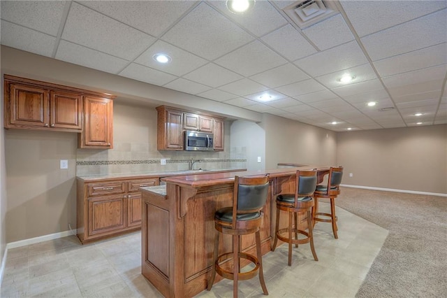 11512 Hadley St, Overland Park, KS 66210 - kitchen featuring stainless steel microwave, brown cabinets, a breakfast bar area, recessed lighting, and a paneled ceiling