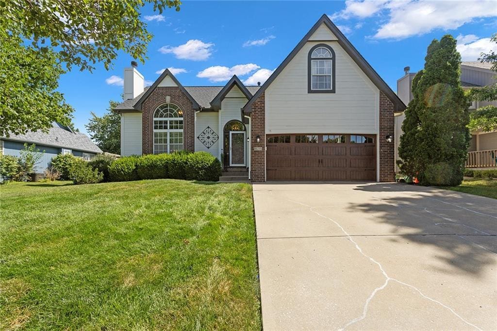 825 12th Ter, Lees Summit, MO 64081 - view of front of property featuring brick siding, a front lawn, concrete driveway, a chimney, and a garage