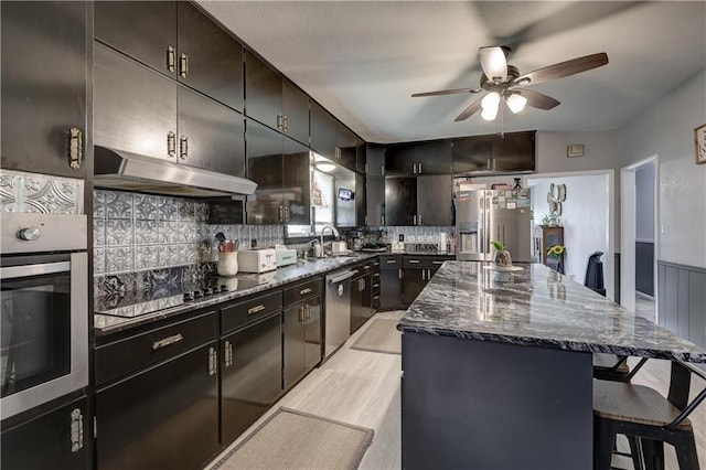 2509 E 4th St, Pittsburg, KS 66762 - kitchen with stainless steel appliances, under cabinet range hood, ceiling fan, a center island, and dark stone counters