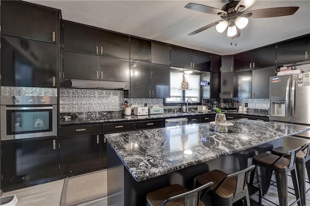 2509 E 4th St, Pittsburg, KS 66762 - kitchen with appliances with stainless steel finishes, under cabinet range hood, ceiling fan, a kitchen breakfast bar, and tasteful backsplash