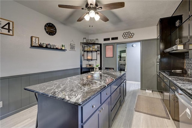 2509 E 4th St, Pittsburg, KS 66762 - kitchen with light wood-style floors, a kitchen island, ceiling fan, dark stone countertops, and a wainscoted wall