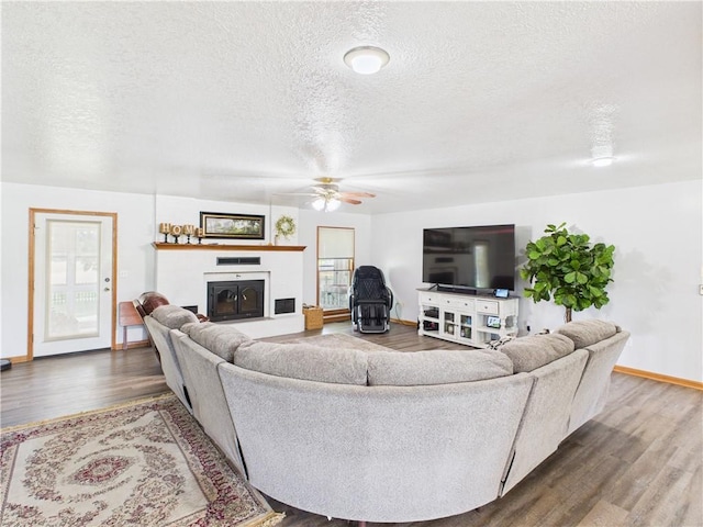 529 SE Dd Hwy, Warrensburg, MO 64093 - living room with wood finished floors, a textured ceiling, a glass covered fireplace, and ceiling fan