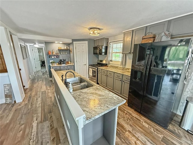 26240 Lakeview Dr, Maryville, MO 64468 - kitchen with black appliances, gray cabinets, wood finished floors, a kitchen island with sink, and light stone counters