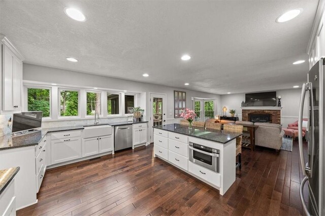 6710 Broadmoor St, Overland Park, KS 66204 - kitchen featuring stainless steel appliances, open floor plan, white cabinets, dark wood finished floors, and a fireplace