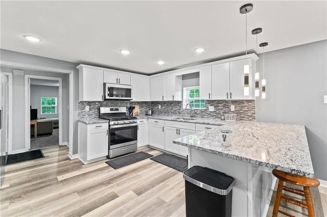 5510 Lafayette Ave, Kansas City, KS 66104 - kitchen featuring gas stove, a peninsula, a breakfast bar, white cabinetry, and backsplash