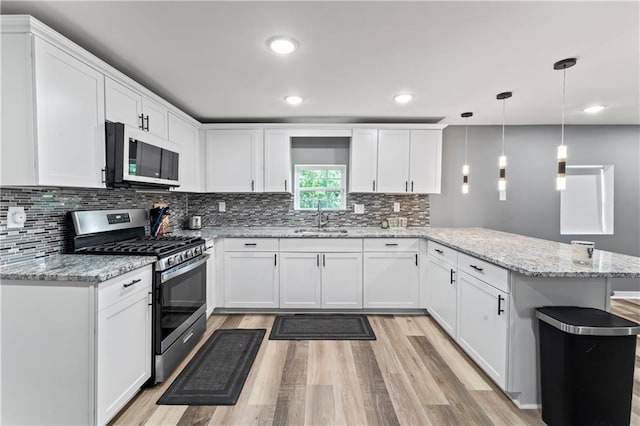5510 Lafayette Ave, Kansas City, KS 66104 - kitchen featuring stainless steel appliances, a peninsula, light wood finished floors, white cabinets, and backsplash