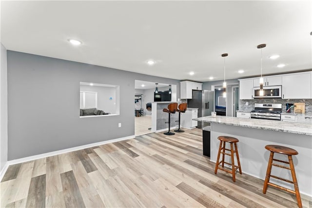 5510 Lafayette Ave, Kansas City, KS 66104 - kitchen featuring appliances with stainless steel finishes, a breakfast bar, light wood finished floors, white cabinetry, and decorative backsplash