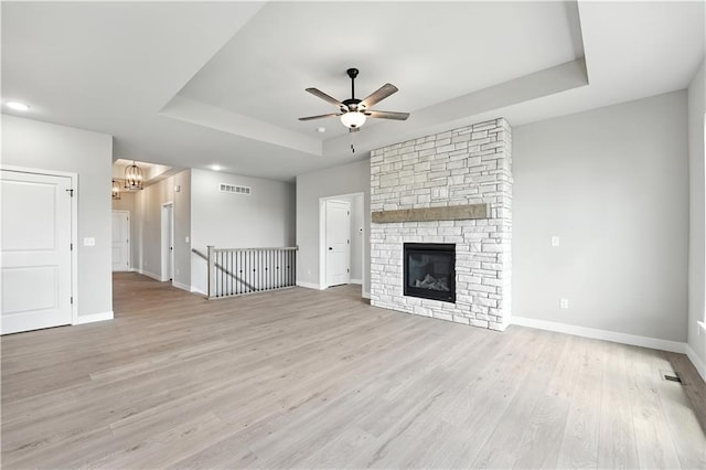 3319 N 109th Ter, Kansas City, KS 66109 - unfurnished living room with a tray ceiling, a ceiling fan, light wood-type flooring, a chandelier, and a stone fireplace